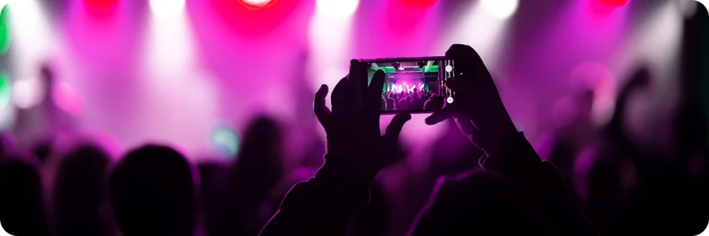 Iemand houdt een smartphone omhoog om een ​​kleurrijk concert vast te leggen. Wazige roze en paarse podiumlichten creëren een levendige en energieke sfeer.